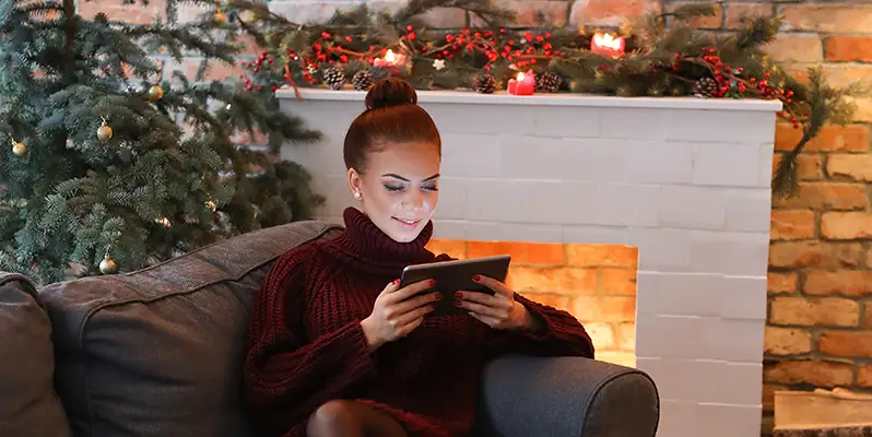 Woman on tablet in front of Christmas tree